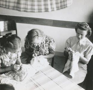 876912 Groepsportret van drie jonge vrouwen die een handwerkles volgen tijdens hun opleiding tot sociaal werkster bij ...